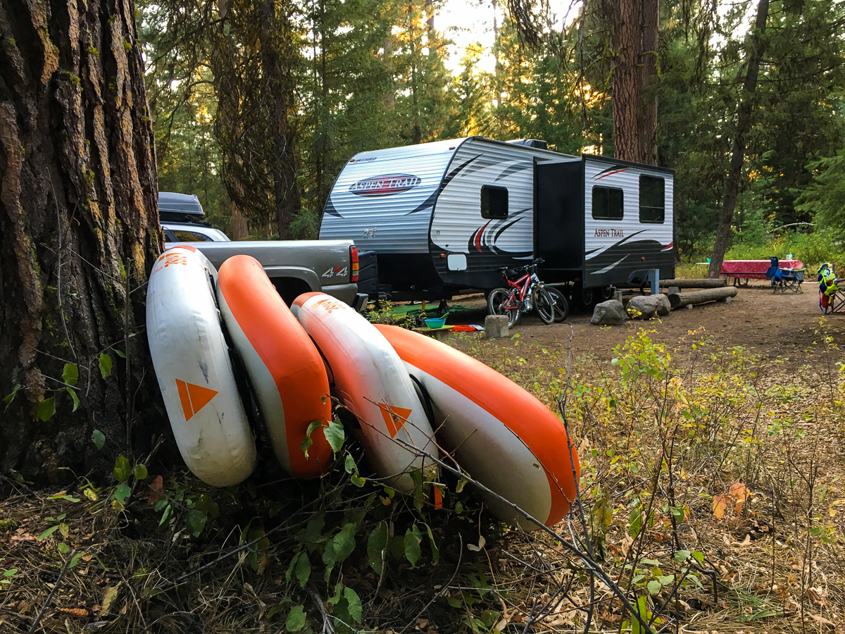 Four Stand Up Paddle Boards (SUP Boards) leaning against a tree in Ponderosa State Park near McCall Idaho. Campsite with a camper, bikes, and picnic table. In the forest with Ponderosa trees.