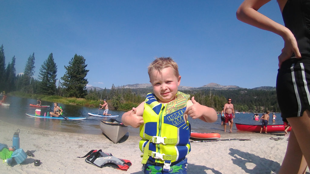 3 year old paddle boarder gives a thumbs up after a long day on the river at the take out point at Payette Lake near McCall Idaho SUP boarding.