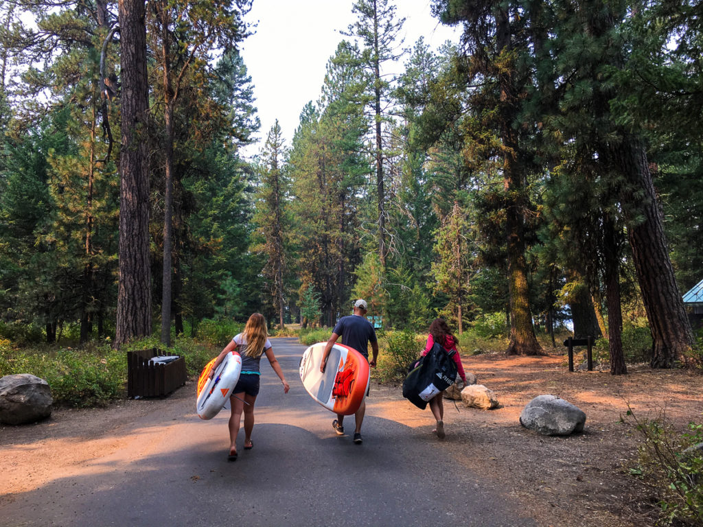 A Family carrying inflatable sup boards on a pathway in McCall's Ponderosa State Park.